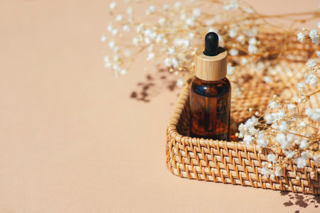 Amber bottle with dropper pipette in a wicker basket. Beige background with daylight and beautiful shadows. Skincare serum or essential oil natural cosmetic. Beauty concept for face and body careの写真素材