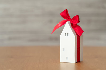 Concept of business in real estate, mortgage, rent. Miniature white house with ribbon bow as a gift on wooden table. Scandi-Boho decoration.の写真素材
