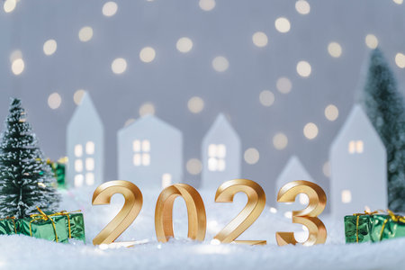 Golden numbers of year 2023. Glowing festive garland with bokeh on light background. Happy New Year greeting card. Cozy atmosphere with cute little house with tree in snow on the backgroundの写真素材