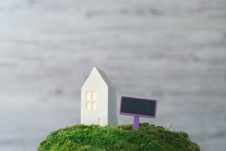 Blank real estate sign in front of house. Concept of sale, mortgage or rent. Miniature white house with a tablet for text on green grass.の写真素材