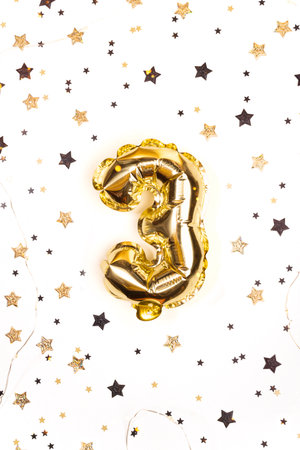 Helium golden balloon number 3. Glowing festive garland with stars confetti. Birthday greeting card. Three-year anniversary backgroundの写真素材