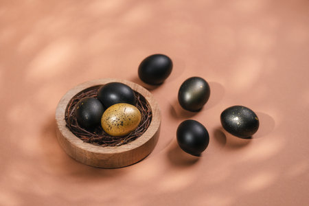 Eggs painted black and gold on biege background. Nest containing three egg. Minimal Easter concept with copy space for text.の写真素材