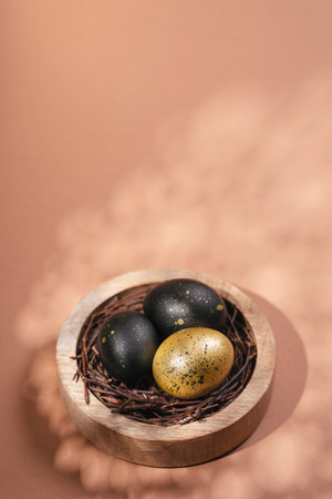 Eggs painted black and gold on biege background. Nest containing three egg. Minimal Easter concept with copy space for text.の写真素材