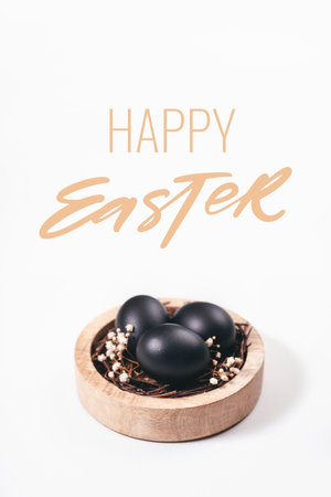 Eggs painted black on white background. Nest containing three egg with gypsophila flowers. Happy Easter greeting card.の写真素材