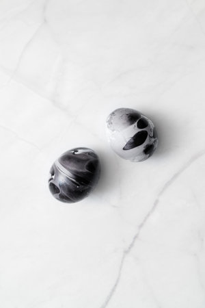 Easter egg decorating ideas. Two eggs painted marble on white background. Minimal Easter concept with space for text. Black monochrome luxury backdrop.の写真素材