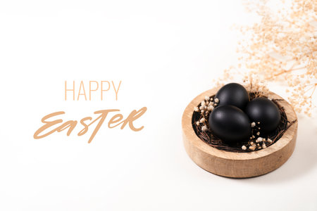 Eggs painted black on white background. Nest containing three egg with gypsophila flowers. Happy Easter greeting card.の写真素材