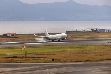 A white airplane landing touch down at Osaka airport, Japan beside the sea and mountainの写真素材