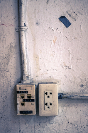 The grunge electric and network plug on the aged white wall with color toned