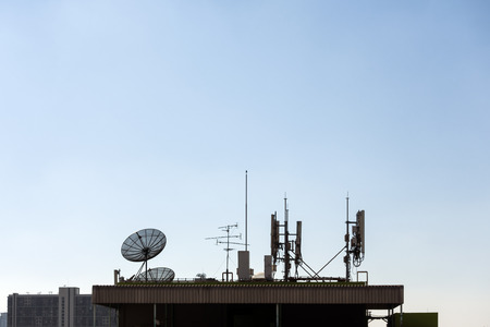 A group of telecomunication antenna and satellite dish on the roof of building with blue sky backgroundの写真素材