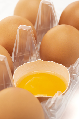 A close-up of an eggs packaging with one crack egg perspective on white background portraitの写真素材