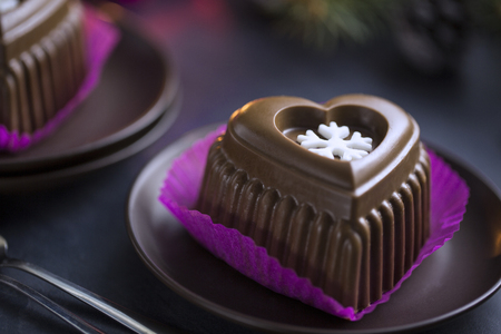 Chocolate Heart Cake with White Snowflake for New Year's Eve. Cake in the purple paper Punnet on the Black Table with Christmas Tree, Candles.の写真素材