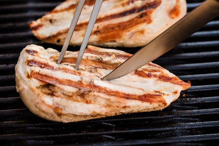Grilled chicken breast fillets on BBQ with fork and knifeの写真素材