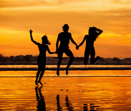 Silhouettes of happy young friends jumping on the beach  against red sunset