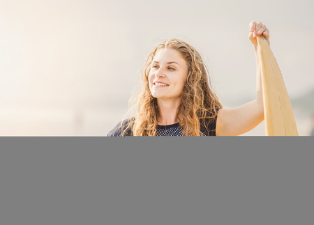 Beautiful young surfer girl stays on the beach at sunset with yellow surfboard. Healthy lifestyle, leisure, travel, holiday and sport concept, copyspaceの写真素材