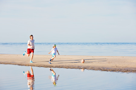 Happy father and son play soccer or football on the beach having great family time on summer holidays. Lifestyle, vacation, happiness, joy conceptの写真素材
