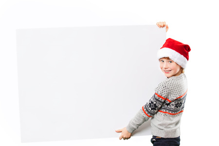 Portrait of a smiling boy in red christmas hat with happy and joyful facial expression holding big empty horizontal blank in hands, isolated on white.の写真素材