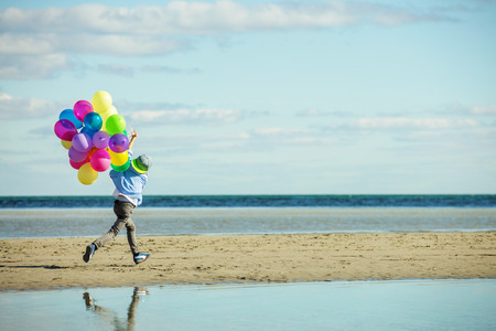 Happy boy plays with colored balloons on the beach having great holidays time on summer. Lifestyle, vacation, happiness, joy conceptの写真素材