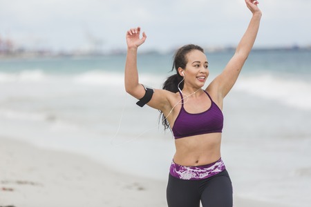 Runner woman running on beach smiling happy. Beautiful vivacious woman jogging on the beach with cloudy wetherの写真素材