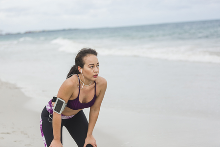 Runner woman resting after long run on the beach. Beautiful vivacious woman jogging on the beach with cloudy weatherの写真素材