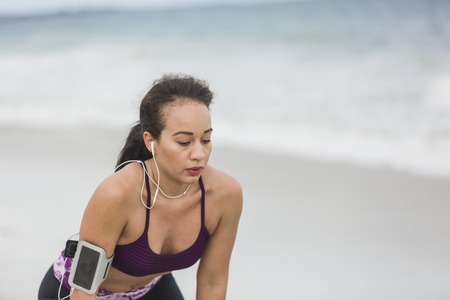 Runner woman resting after long run on the beach. Beautiful vivacious woman jogging on the beach with cloudy weatherの写真素材