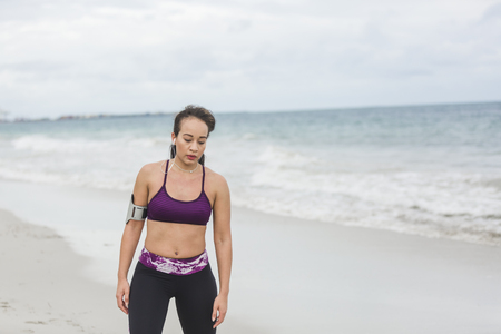 Runner woman finishing work out on beach smiling happy. Beautiful vivacious woman jogging on the beach with cloudy weatherの写真素材