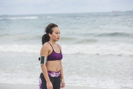 Runner woman resting after long run on the beach. Beautiful vivacious woman jogging on the beach with cloudy weatherの写真素材