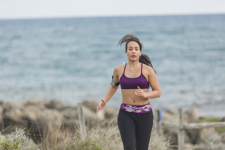 Portrait of young sports woman in fitness outfit jogging by the beach at cloudy winter dayの写真素材