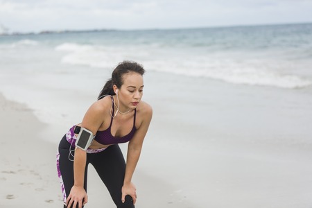 Runner woman resting after long run on the beach. Beautiful vivacious woman jogging on the beach with cloudy weatherの写真素材