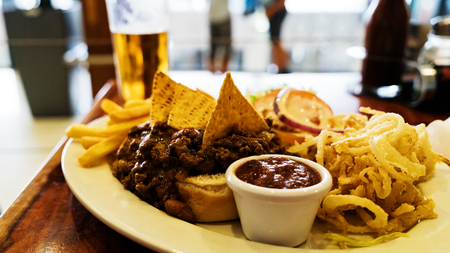 Unhealthy meal with mexican nacho chips loaded with beef, cheese, fries, onion rings and hot souseの写真素材