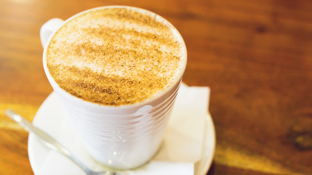 Fresh cappuccino cup with spoon on the brown wooden table. Closeupの写真素材