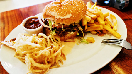 Unhealthy meal with mexican nacho chips, beef burger, loaded with cheese, fries, onion ringsの写真素材