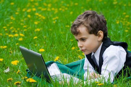 Seven years old businessman with his laptop on a meadow