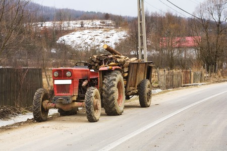 Red tractor with rusty trailer loaded with logsの写真素材
