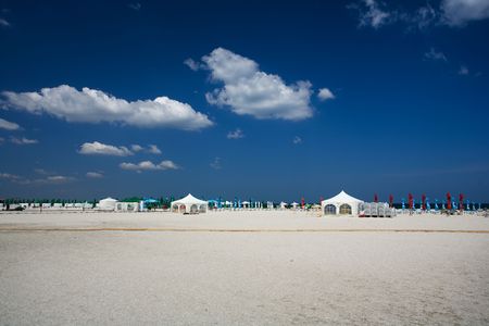 Landscape at seaside with tents and umbrellas on the beach, under blue sky with fluffy cloudsの写真素材