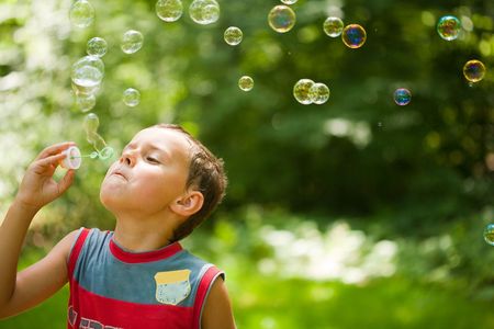 Cute kid blowing bubbles outdoors, in the forest in a beautiful sunny afternoonの写真素材