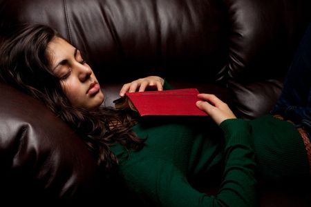 Beautiful young lady fallen asleep after reading a book, on a leather sofaの写真素材