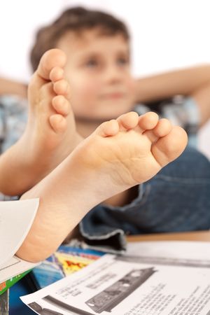 Portrait of a barefoot schoolboy with his feet up on his desk, waiting for holiday to comeの写真素材