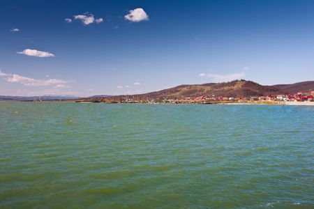 Landscape with a dam or barrage near a village and hills in the background, under beautiful blue sky