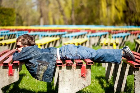 Kid lying on benches in a park in a sunny dayの写真素材