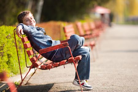 Cute schoolboy relaxing sitting on bench in a parkの写真素材