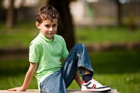 Portrait of a cute little boy sitting on a bench in a parkの写真素材