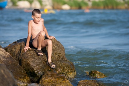 Cute kid sitting on rocks near sea shoreの写真素材