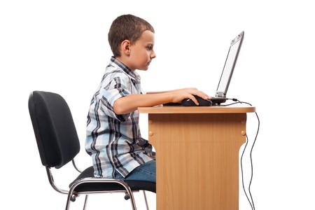 Cute schoolboy sitting at his laptop doing homework or playing, isolated on white background