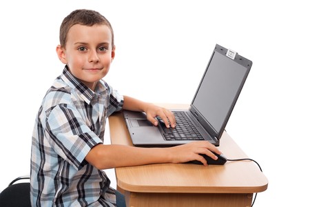 Cute schoolboy sitting at his laptop doing homework or playing, isolated on white background