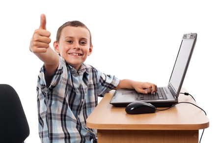 Cute schoolboy sitting at his laptop doing homework or playing, isolated on white background