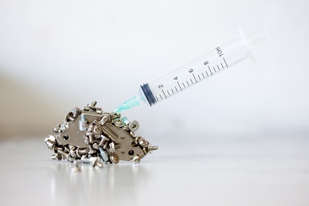 Syringe plunged into a pile of small computer nuts and boltsの写真素材