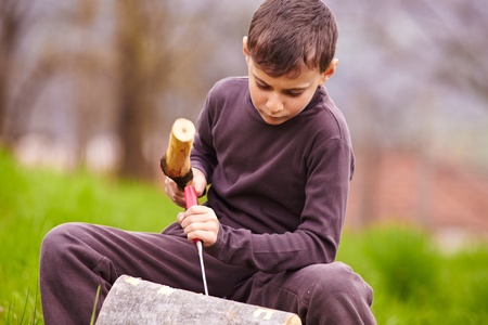 Boy sculpting with a chisel into the bark of a beech log outdoorの写真素材