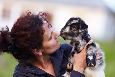 Portrait of a young woman holding a baby goat outdoorの写真素材