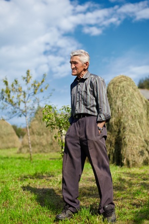 Full length portrait of a senior farmer on a meadow with hay stacks in backgroundの写真素材