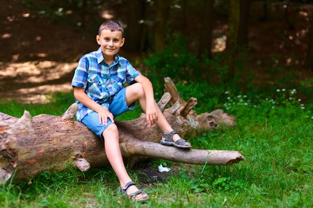 Happy boy outdoor in the forest, resting on a fallen tree trunkの写真素材